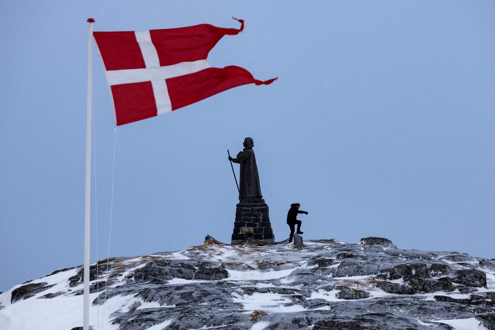 Det danske flagget vaier foran den omstridte statuen av den norske misjonæren Hans Egede på toppen av Grønlands hovedstad Nuuk.
